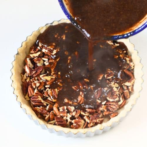 Pouring the pecan pie mixture on the pecans in the crust.