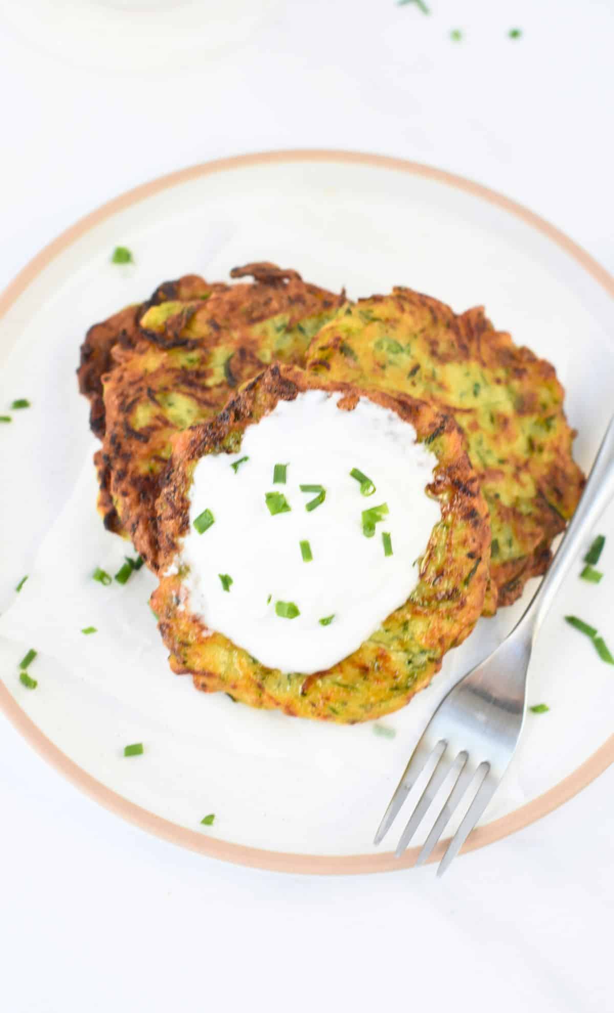 Vegan Zucchini Fritters on a plate, served with vegan sour cream and chives.