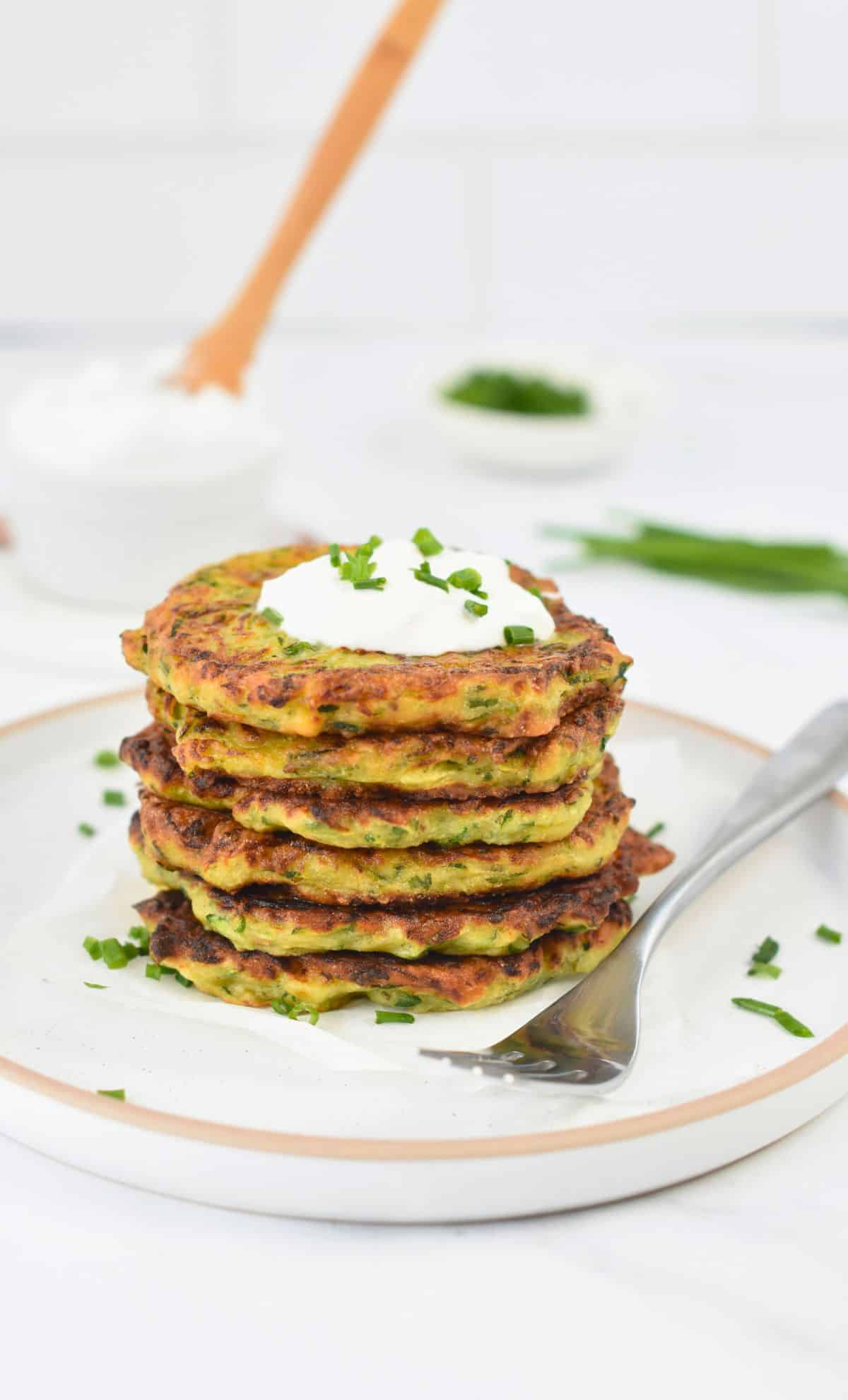 Vegan Zucchini Fritters stacked on a white plate.