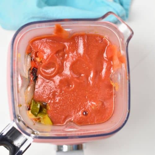 Roasted veggies in a blender covered with marinara sauce.