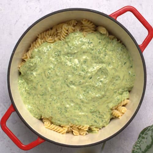 Adding the green sauce to pasta in a pan.