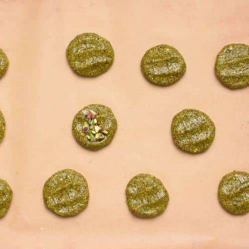 Flattened pistachio cookies on a baking sheet.