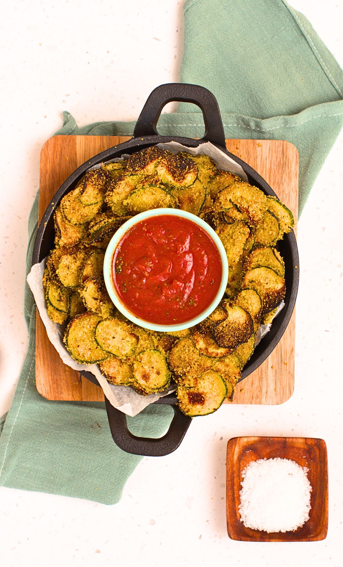 Baked zucchini on a cast-iron pan with ketchup in a ramekin.