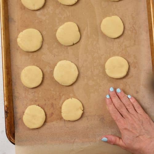 Flattening 3-Ingredient Sugar Cookies on a cookie sheet.