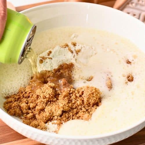 Pouring cider in dry Apple Cider Donut Holes ingredients.