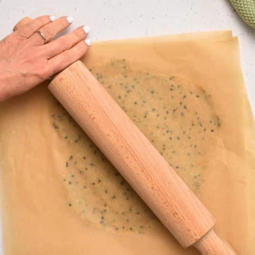 Flattening the Almond Flour Cracker dough ball between pieces of parchment paper.