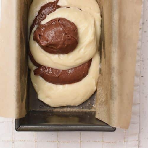 Four dollops of alternating Marble Pound Cake batter in a loaf pan.