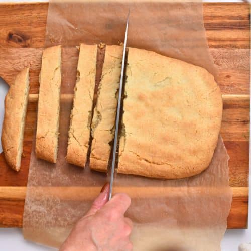 Slicing pre-cooked Almond Flour Biscotti on a chopping board.