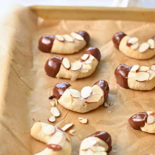 Almond Horns Cookies decorated with chocolate and almond slices on a baking sheet.