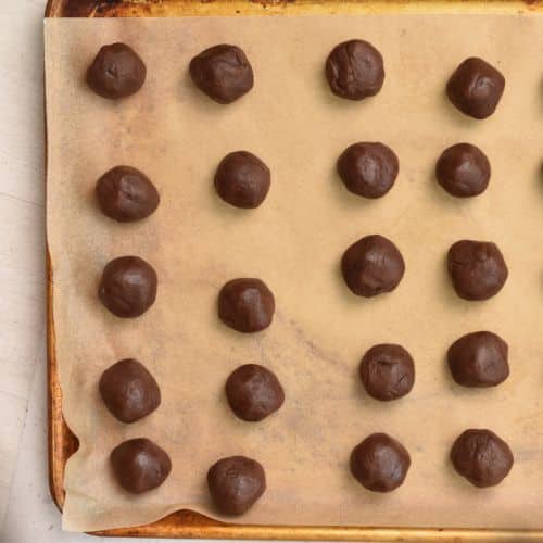 Rolled Chocolate Thumbprint Cookie dough balls on a baking sheet.