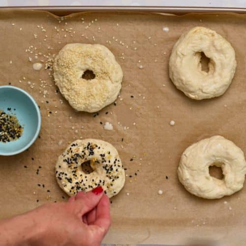 Decorating 2-Ingredient Bagels with bagel seasoning on a baking sheet.