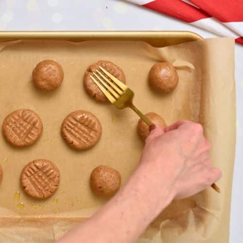 Flattening the Almond Butter Cookies with a fork on a baking sheet.