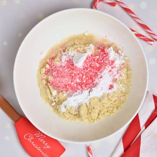 Crushed candy cane on Almond Candy Cane Cookie ingredients in a mixing bowl.