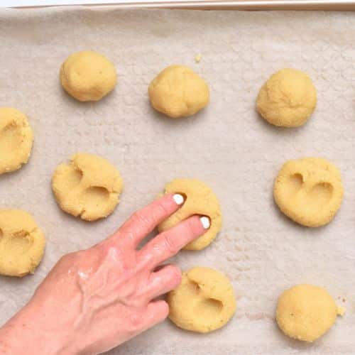 Pressing two fingers to flatten the cookie balls and make two cavities on the cookies.