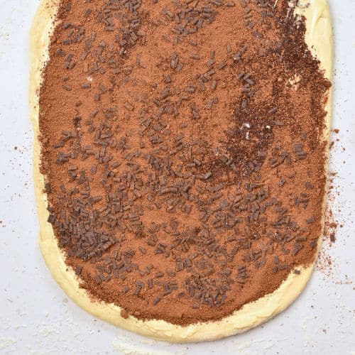 Cocoa powder sugar mixture and chocolate chips spread on the Chocolate Cinnamon Roll dough.