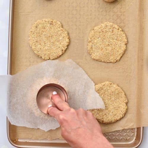 Flattening Crispy Oatmeal Cookies with a measuring cup.