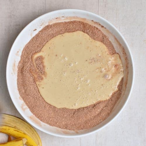 Poured banana milk on the Healthy Chocolate Muffin dry ingredients in a bowl.