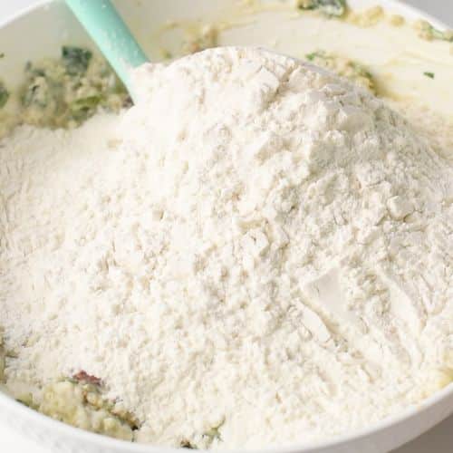 Adding flour to the Quinoa Biscuit base ingredients in a bowl.