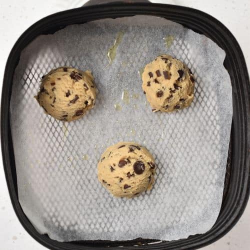 Air fryer Chocolate Chip Cookie dough balls in an air fryer basket.