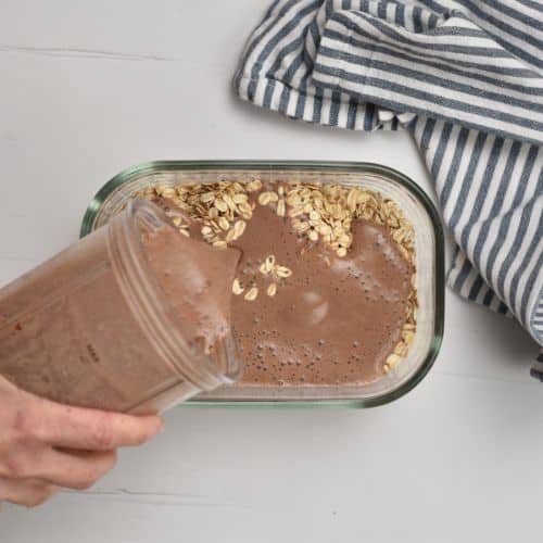 Pouring chocolate milk on the dry Banana Chocolate Overnight Oats mixture.